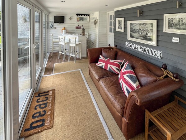 A cozy living area with a leather sofa, a coffee table, and a dining table with chairs. There are framed pictures on the wall and a television above the dining table. - 3 bedroom accommodation in Sandilands (Sandilands)