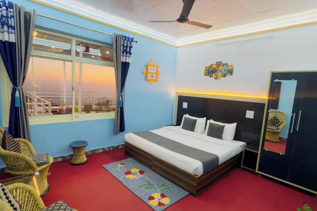 Un dormitorio con una cama, un ventilador de techo, una ventana con cortinas, una silla y una mesita.