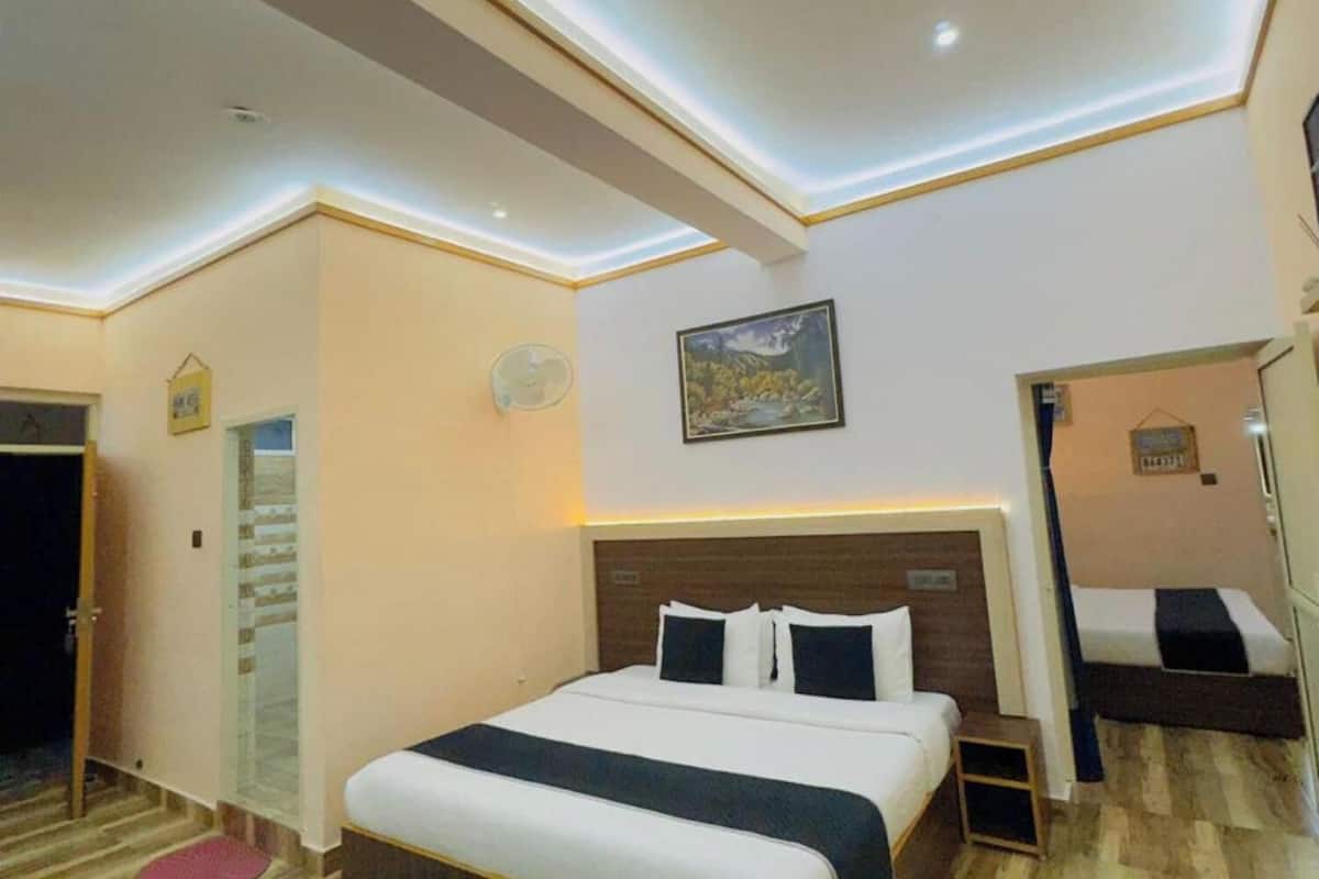 Habitación de hotel con una cama grande, una mesita de noche pequeña, un tapete verde y un cuadro en la pared.