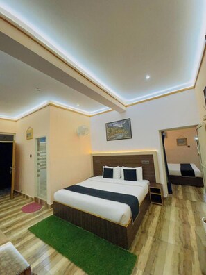 A hotel room with a large bed, a small bedside table, a green rug, and a painting on the wall. - Paradise Inn Dharmsala (Dharamshala)