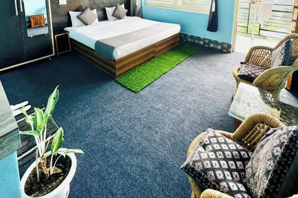 Una habitación de hotel con cama, ventilador de techo, ventana con cortinas, una silla y una mesita.
