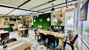 Una cafeteria amb taules i cadires, una paret verda i una vista per la finestra.