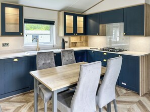 A modern kitchen with dark blue cabinets, a wooden dining table, and grey upholstered chairs.