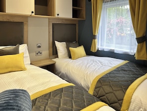 Habitación de hotel con dos camas, cada una con cabecera, mesita de noche y ventana con cortinas.