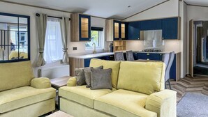 Ein gemütlicher Wohnraum mit Sofa, kleinem Tisch, Küchenzeile und einem Fenster mit Vorhängen.