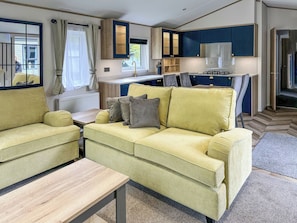 A compact living space with a sofa, a small table, a kitchenette, and a window with curtains.