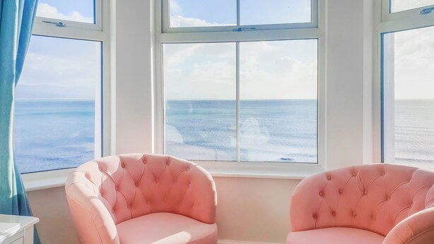 A room with two pink tufted chairs facing a window with a view of the ocean. - Glan Y Mor - UK52092 (Criccieth)
