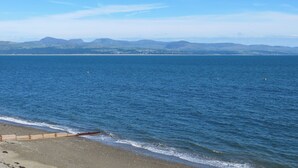 A beach with a wooden structure on the shore, calm sea, and distant mountains. - Glan Y Mor - UK52092 (Criccieth)