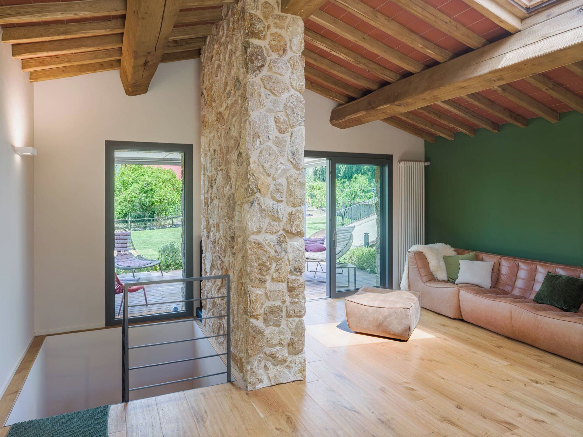A modern living room with a stone pillar, wooden beams, a green wall, and a leather sofa.