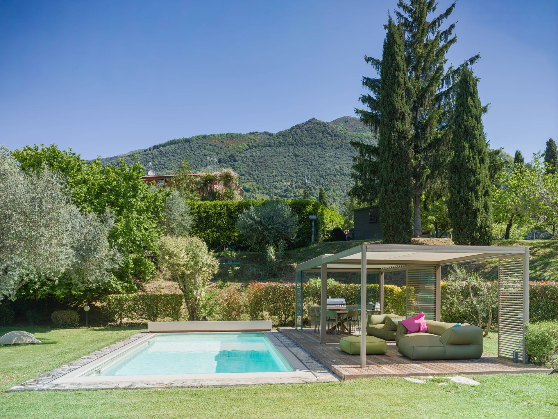 A swimming pool with a wooden deck, outdoor seating, and a mountain backdrop.