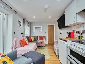 A compact living space with a kitchenette, a sofa with colorful cushions, a small dining table, and a television mounted above the counter. - No.4 Princess Yellow Apartments - UK52100 (Portrush)