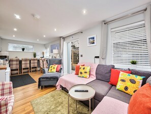 Ein modernes Wohnzimmer mit einer Couch, Sesseln, einem kleinen Tisch und einer Küchenzeile im Hintergrund.