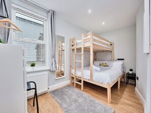 A bunk bed room with a radiator, a grey rug, and a small table with a plant. - No.4 Princess Yellow Apartments - UK52100 (Portrush)