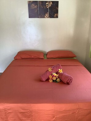 Una cama con una colcha roja, dos almohadas y una toalla con motivos florales.