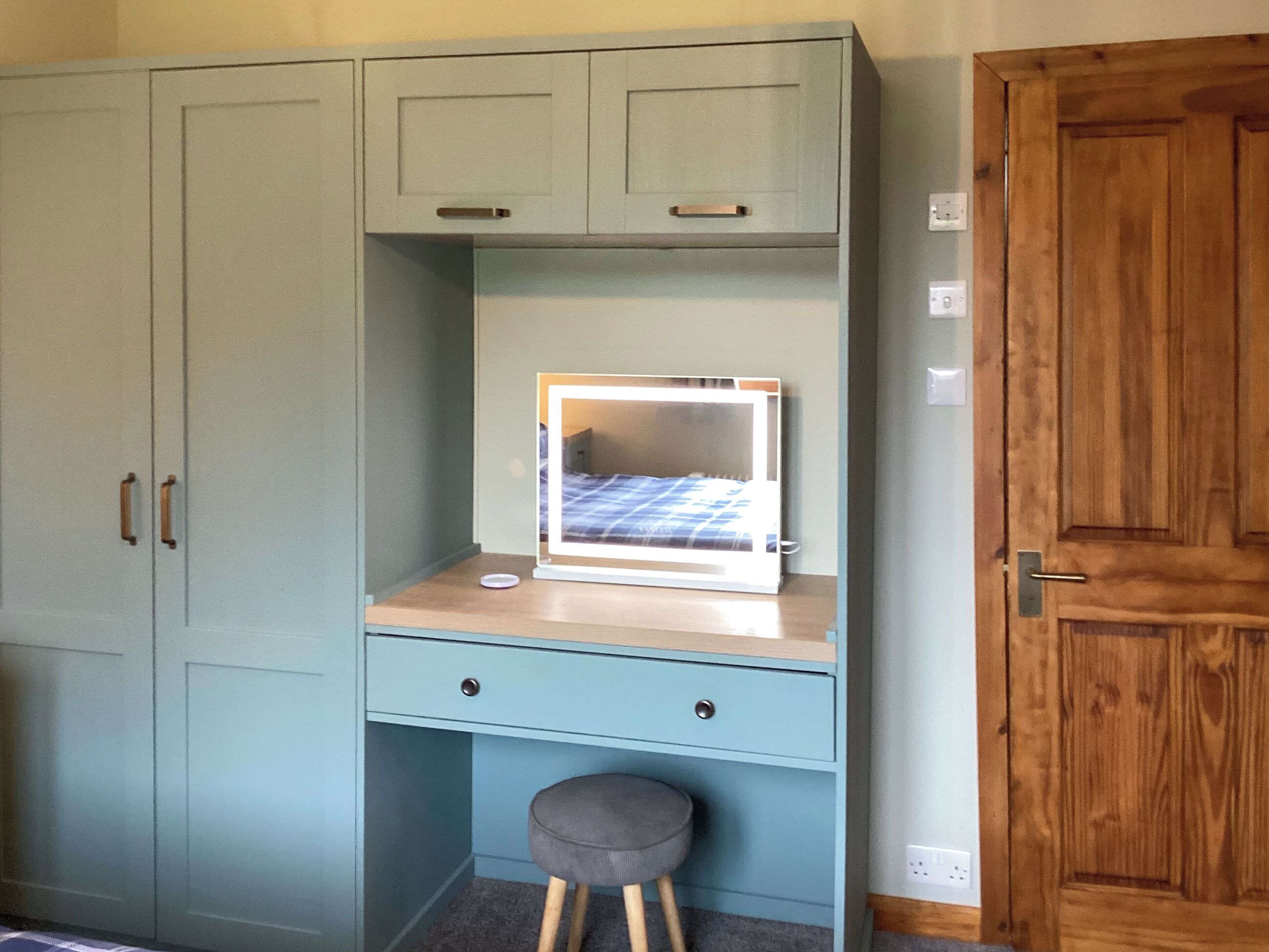A room with a light blue desk, a mirror, a stool, and a wardrobe.