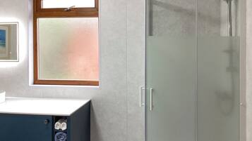 A bathroom with a glass shower enclosure, a wooden-framed window, and a white sink with towels.