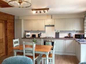 A kitchen with white cabinets, a wooden dining table, and a ceiling light fixture. - 1 bedroom accommodation in Brora (Brora)