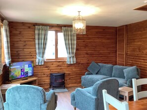 A cozy cabin interior with a TV, sofa, and a wood-burning stove. - 1 bedroom accommodation in Brora (Brora)