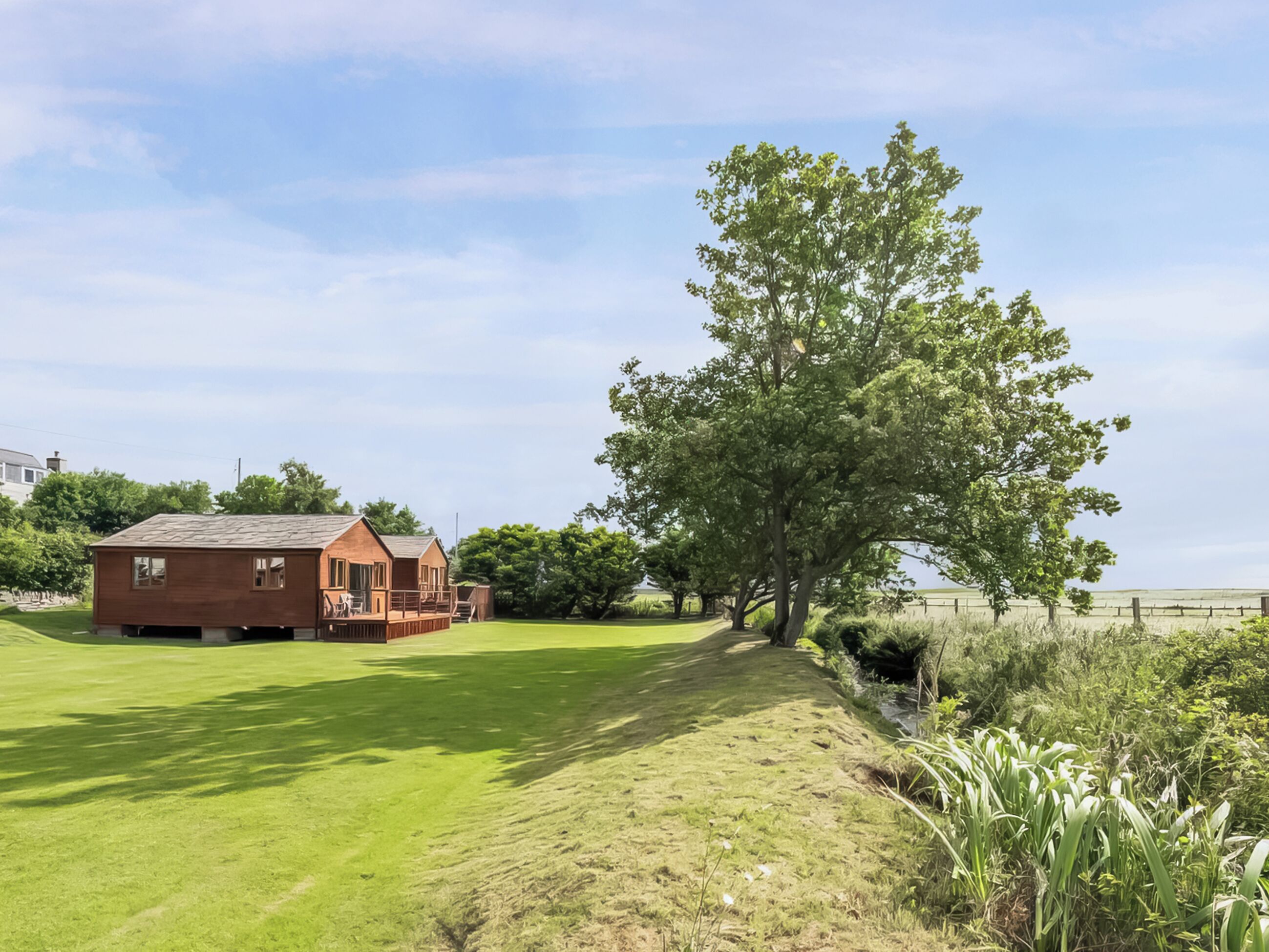 A single-story brick building with a deck, surrounded by a well-maintained lawn and a large tree.