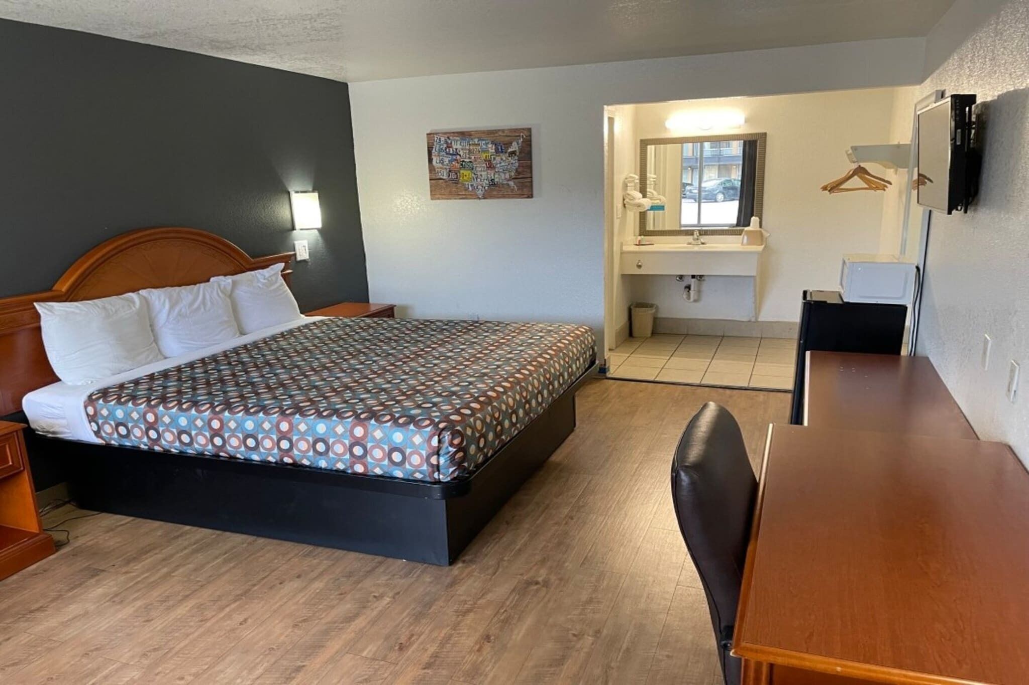 A hotel room with a bed, a desk, a chair, a bathroom with a mirror, and a wall-mounted TV.
