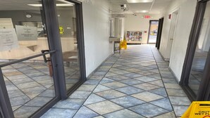 A hallway with tiled flooring, glass doors, an exit sign, and a caution wet floor sign.