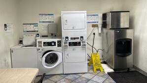A laundry room with stacked washers and dryers, a water cooler, and caution signs.