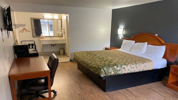 A hotel room with a bed, desk, chair, and a bathroom with a mirror and sink.
