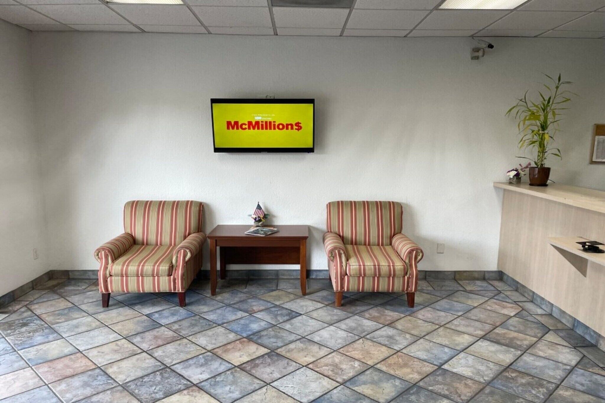 Una hall con due poltrone a righe, un tavolino con una bandiera americana, un cartello McDonald's e una pianta in vaso.