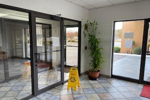 A hotel entrance with glass doors, a caution sign, a potted plant, and a red mat.