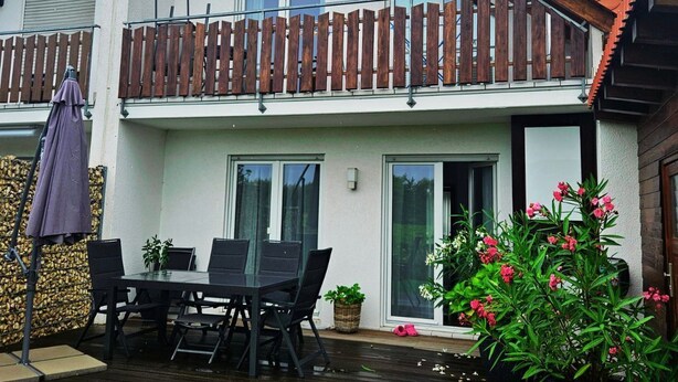 En tvåvåningsbyggnad med en balkong, ett utomhusområde med sittplatser och krukväxter.