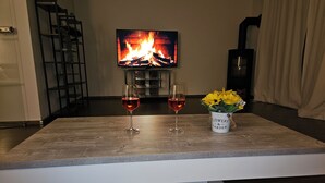 Ett vardagsrum med en öppen spis, två vinglas och en vas med blommor på ett träbord.