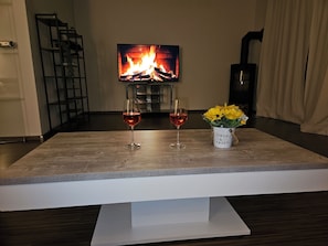 Un salon avec une cheminée, deux verres à vin et un vase de fleurs posé sur une table en bois.