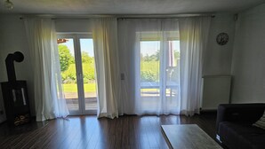 Ett vardagsrum med en öppen spis, en soffa och ett stort fönster med gardiner.