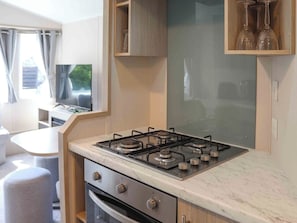 A compact kitchenette with a gas stove, oven, and a small dining area with a table and chairs. - Sarnfaen Static - UK52097 (Tal-y-Bont, near Barmouth)