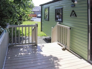 A wooden deck leading to a green building with a stone wall in the background. - Sarnfaen Static - UK52097 (Tal-y-Bont, near Barmouth)