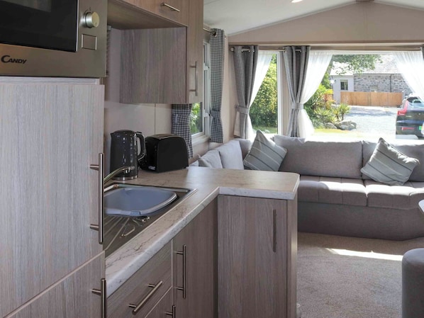 A compact kitchenette with a sink, a coffee maker, and a toaster. There is a sofa with cushions in the adjacent living area. - Sarnfaen Static - UK52097 (Tal-y-Bont, near Barmouth)