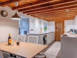 Eine moderne Küche mit Holzbalken, einem Essbereich mit Tisch und Stühlen und Blick ins Freie.