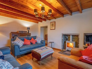 Ein gemütliches Wohnzimmer mit einem blauen Sofa, Holzboden, Kamin und Deckenbalken.