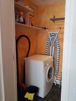A compact laundry room with a washing machine, a drying rack, and a small shelf with cleaning supplies. - Furnished F3 apartment in city center (Châteauroux)