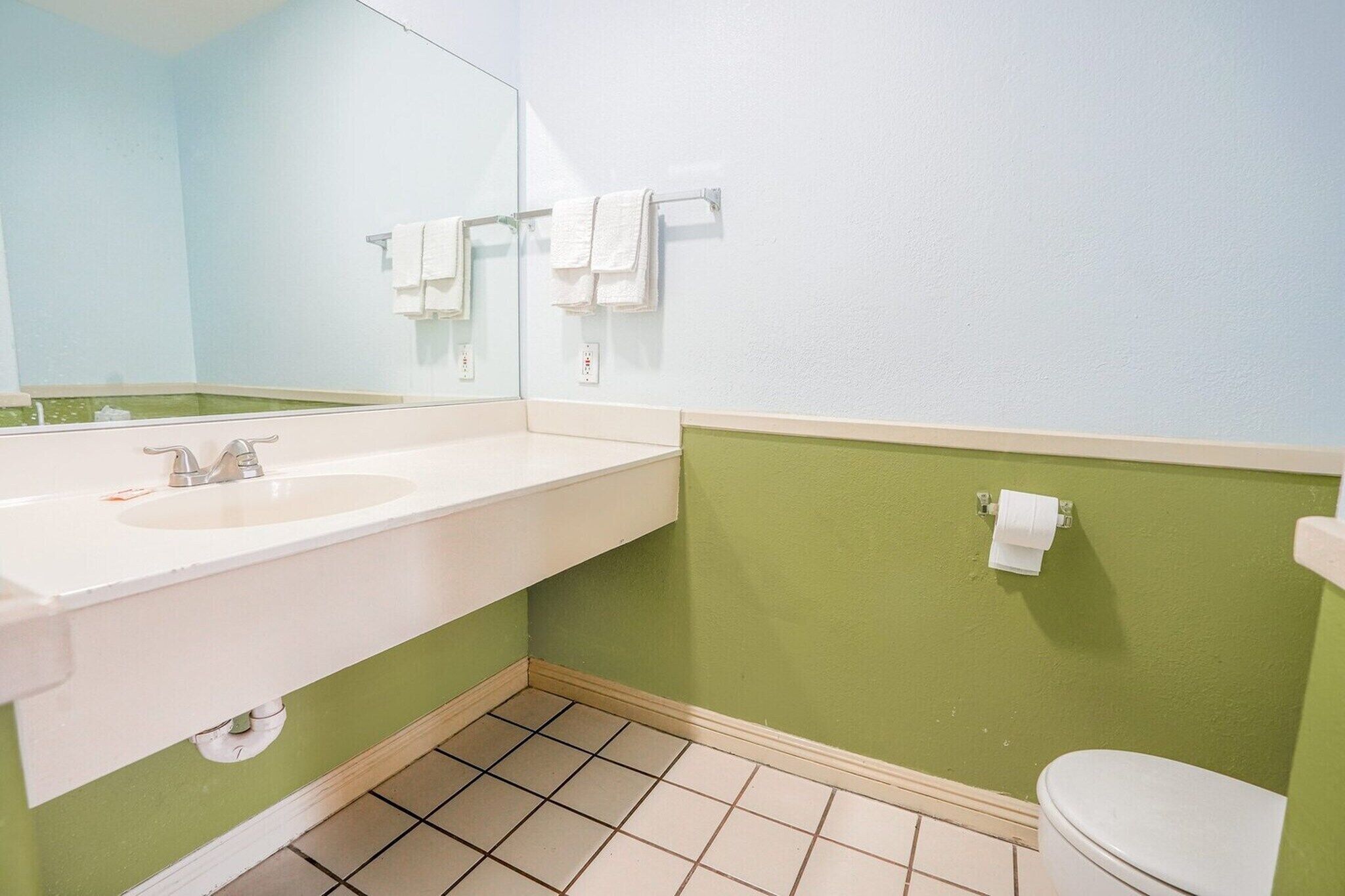 A bathroom with a white sink, a mirror, a toilet, and green walls.