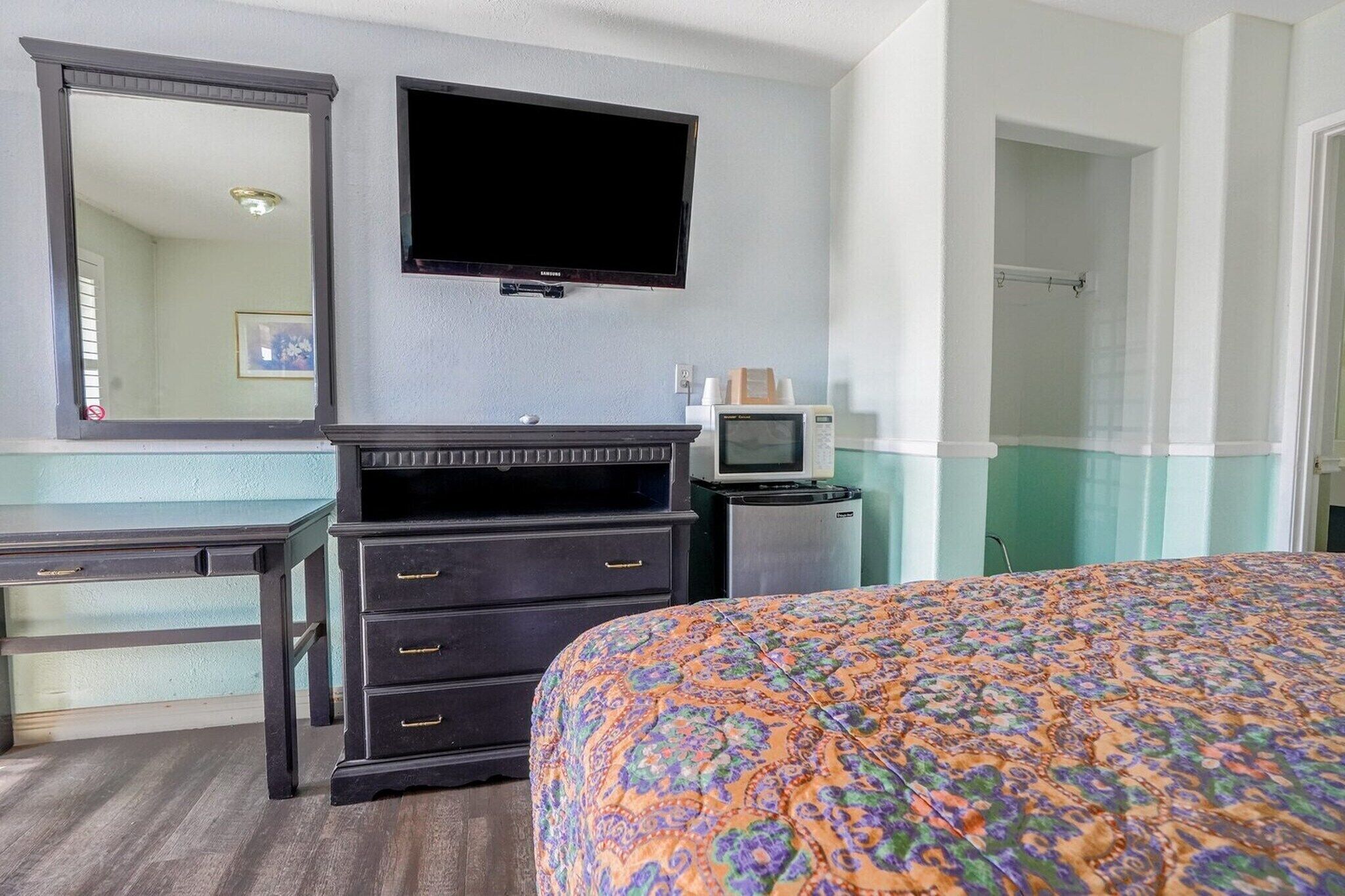 Una habitación de hotel con cama, cómoda, televisor, microondas y puerta que da a un baño.