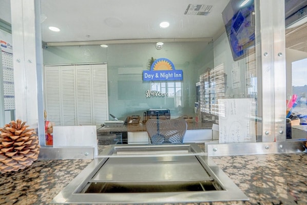Uma área de recepção com o letreiro Day & Night Inn, um balcão de atendimento, uma cadeira e uma decoração com um pinheiro.