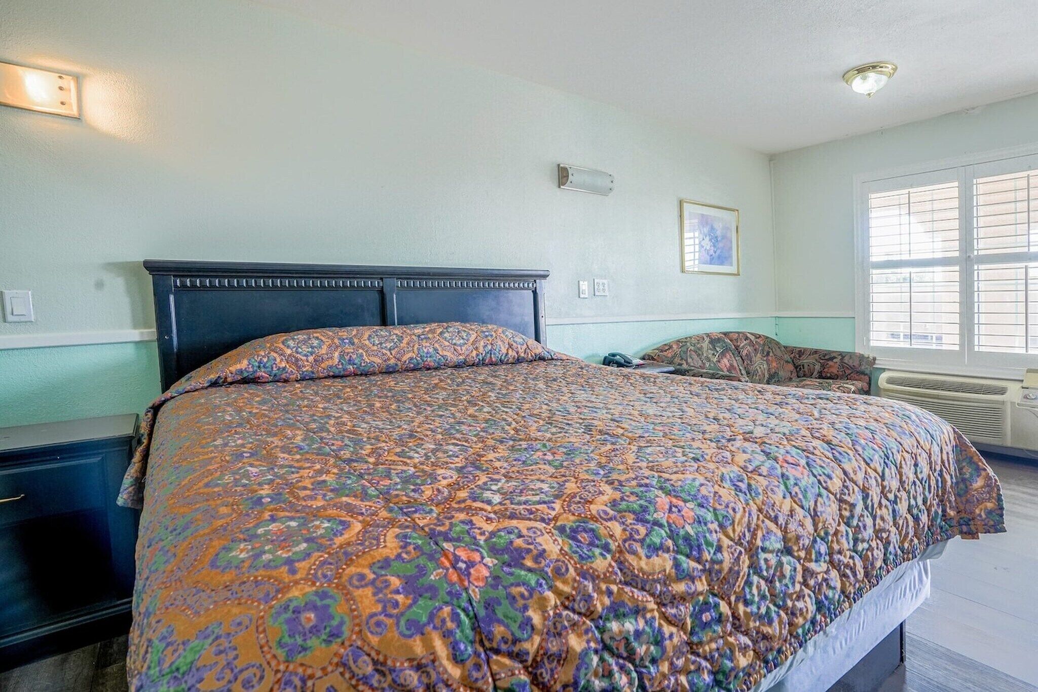 A bedroom with a large bed, a nightstand, a chair, and a window with blinds.