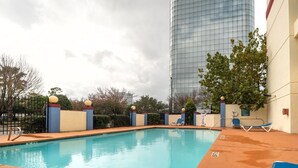Piscina com espreguiçadeiras, um edifício alto ao fundo e céu nublado.