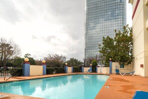 Una piscina con sillas de descanso, un edificio alto al fondo y un cielo nublado.
