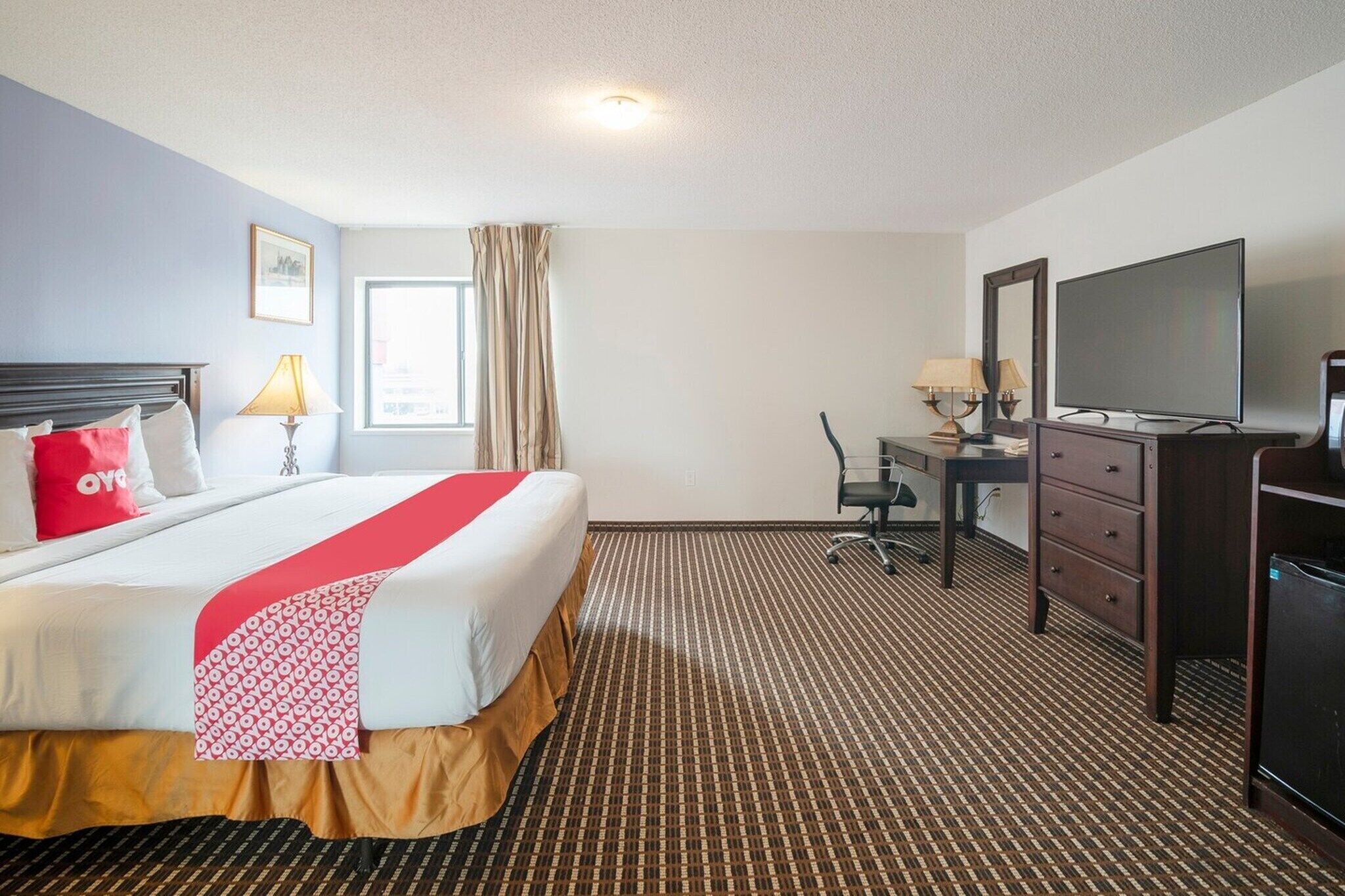 A hotel room with a bed, a desk, a television, and a window with curtains.