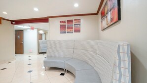 A curved sectional sofa in a hotel lobby with a tiled floor, a painting on the wall, and an exit sign.
