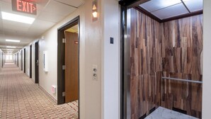 Corredor de hotel com sinalização de saída, parede de madeira e elevador.