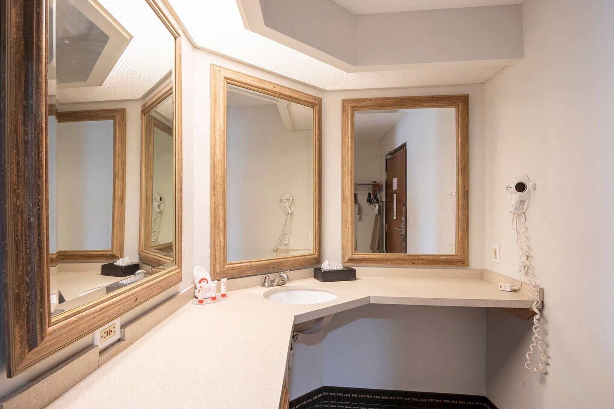 Une salle de bain avec trois miroirs, un lavabo et un sèche-cheveux posés sur une étagère fixée au mur.