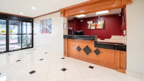 Bancada de recepção com balcão de madeira e topo preto, parede vermelha com obras de arte e piso ladrilhado.